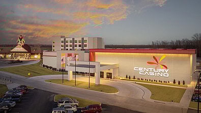 A modern casino building with a large sign reading "CENTURY CASINO," surrounded by parking and a sunset sky.